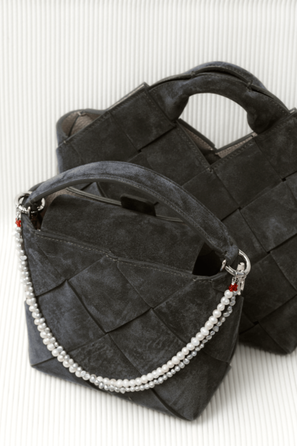 Close-up of a black handbag adorned with a two-layered bag charm of freshwater pearls on a white chair