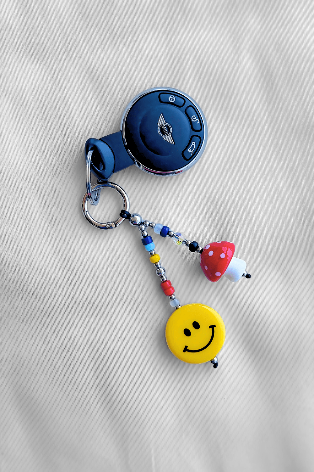 Keychain with car key replica, smiley face charm, and colorful beads on a light gray background