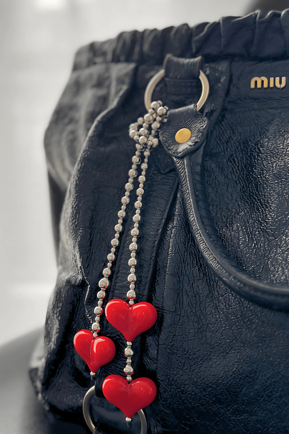 Silver beaded bag charm with red hearts wrapped on a black designer handbag.