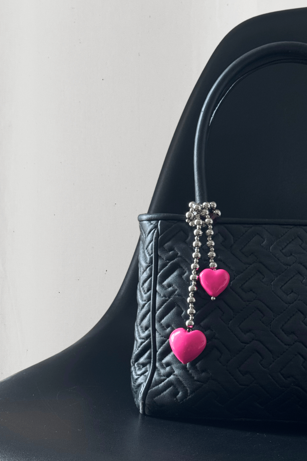 Lifestyle photo of a designer handbag and a silver bead charm with pink hearts.