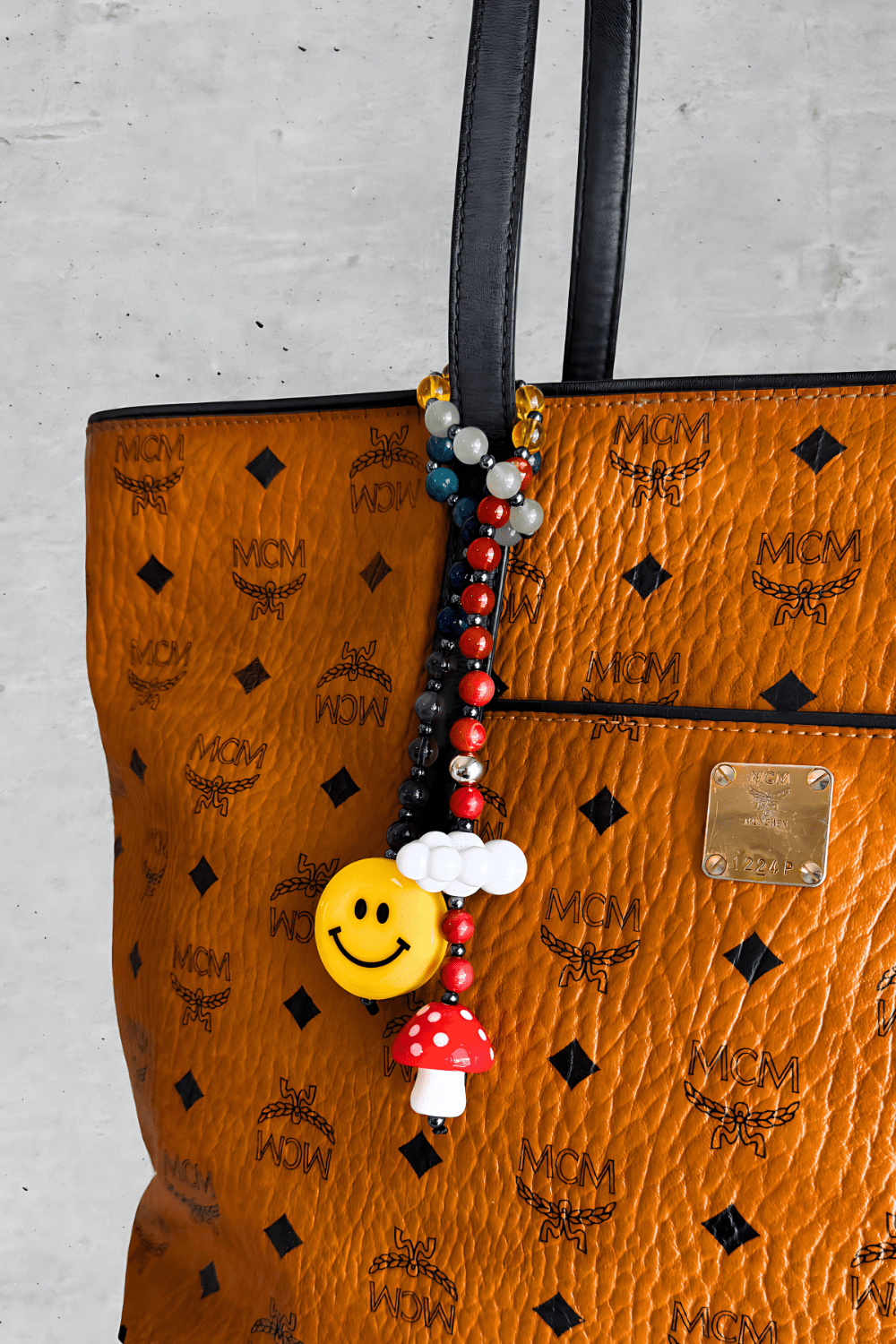 Colorful beaded bag charm with smiley face, mushroom, and cloud - attached to luxury brown MCM handbag handle.
