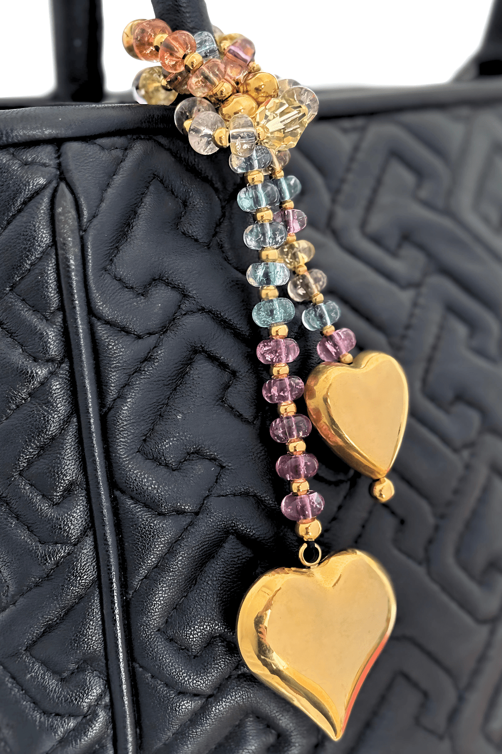 Colorful beaded bag charm with Swarovski crystals and gold hearts wrapped on a black handbag.