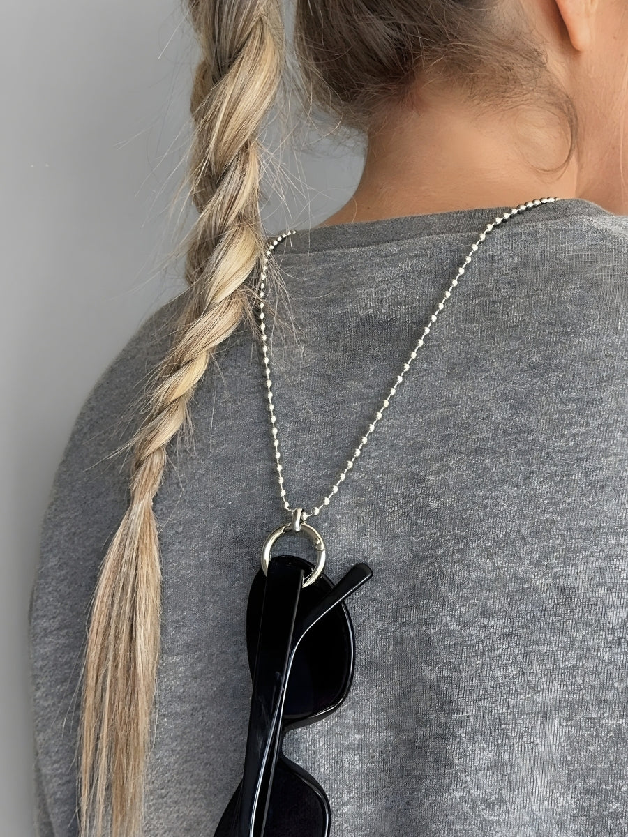 Person wearing a necklace with a pendant holding sunglasses, against a neutral background