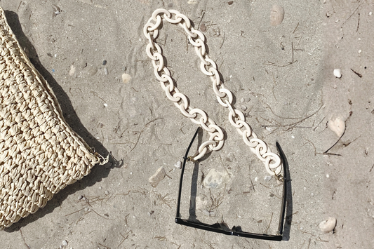 Handcrafted cream resin eyewear chain with sunglasses on sand, featured in SPECSET's Island Hopping Edit blog.