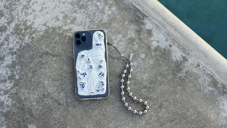A handmade phone case with a silver bracelet attached, laid on a neutral surface.