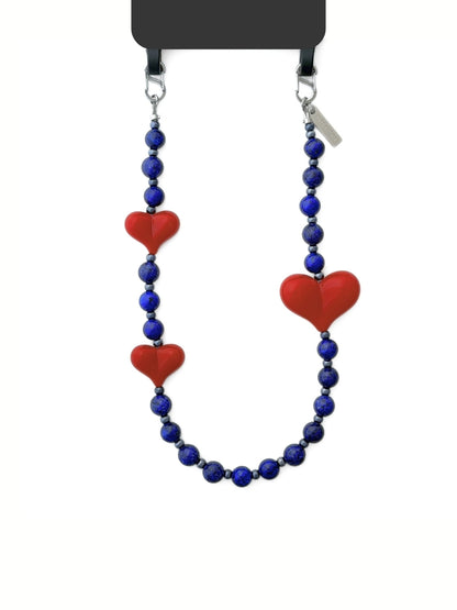 A beaded strap featuring deep blue round beads and three red heart-shaped beads, displayed on a black phone case against a plain white background.