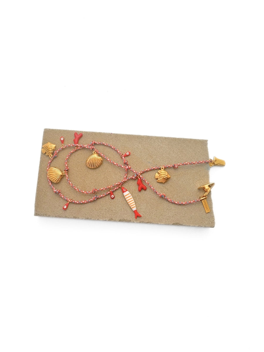 A colorful glasses strap with gold-toned seashell and fish charms, displayed on a textured brown paper card against a white background.