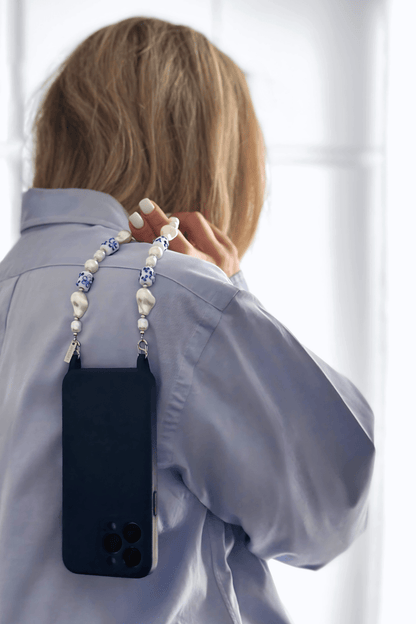 A woman holding a phone with the Greek Chic Phone Strap attached, highlighting its stylish and functional design.