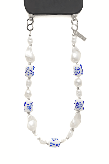 Close-up of the Greek Chic Phone Strap featuring white pearls and blue floral ceramic beads, attached to a phone case with metal clasps.