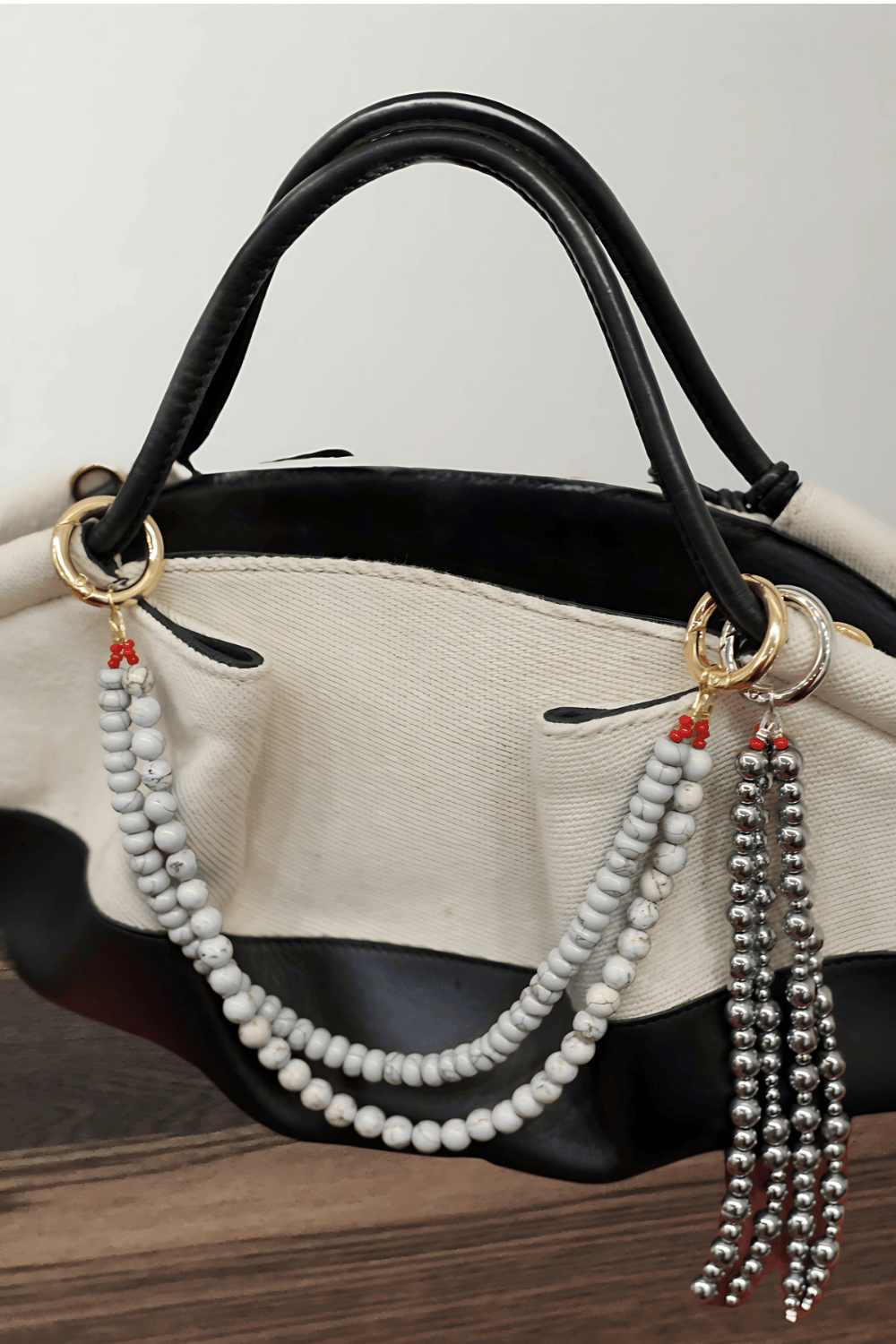 Black handbag with a beaded keychain attached on a wooden surface