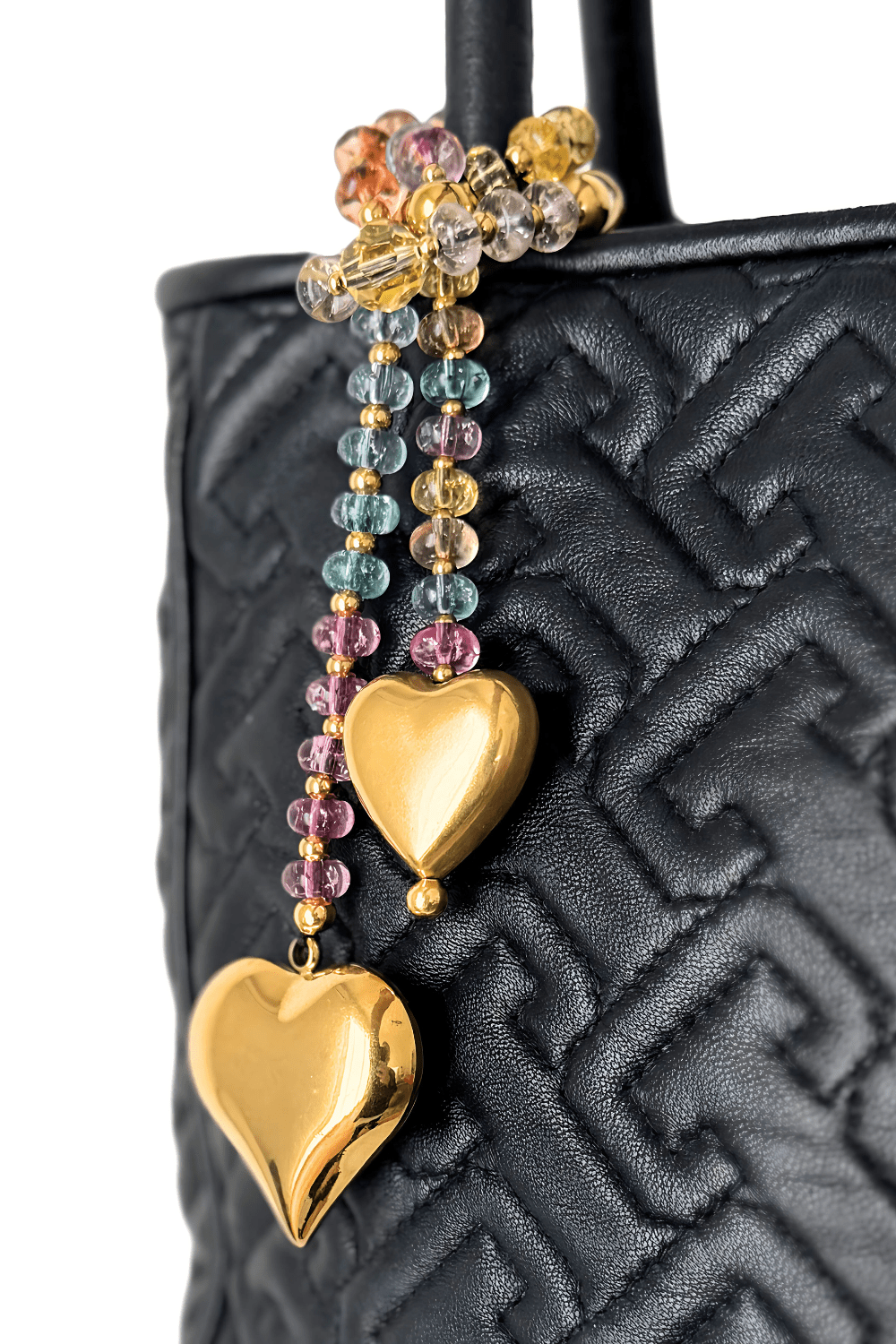 Close-up pastel Swarovski crystal bag charm  with gold hearts on a black handbag.