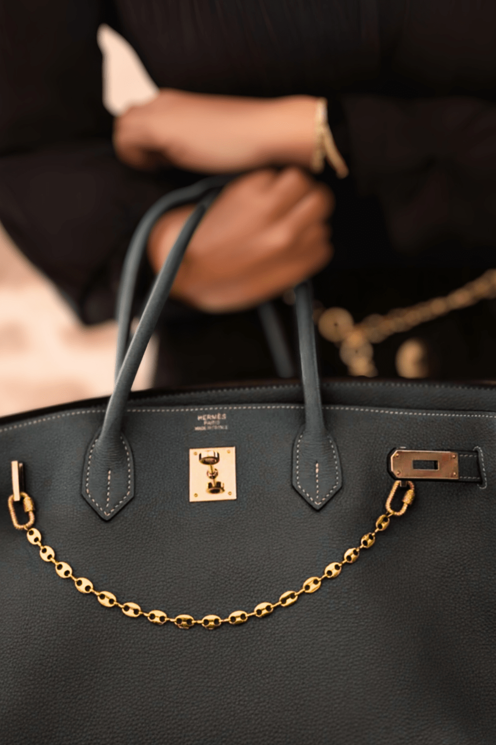 Common Link Chain clipped as a designer Bag Charm on a gray leather handbag, showcasing the high-polish gold links and sparkling clips.