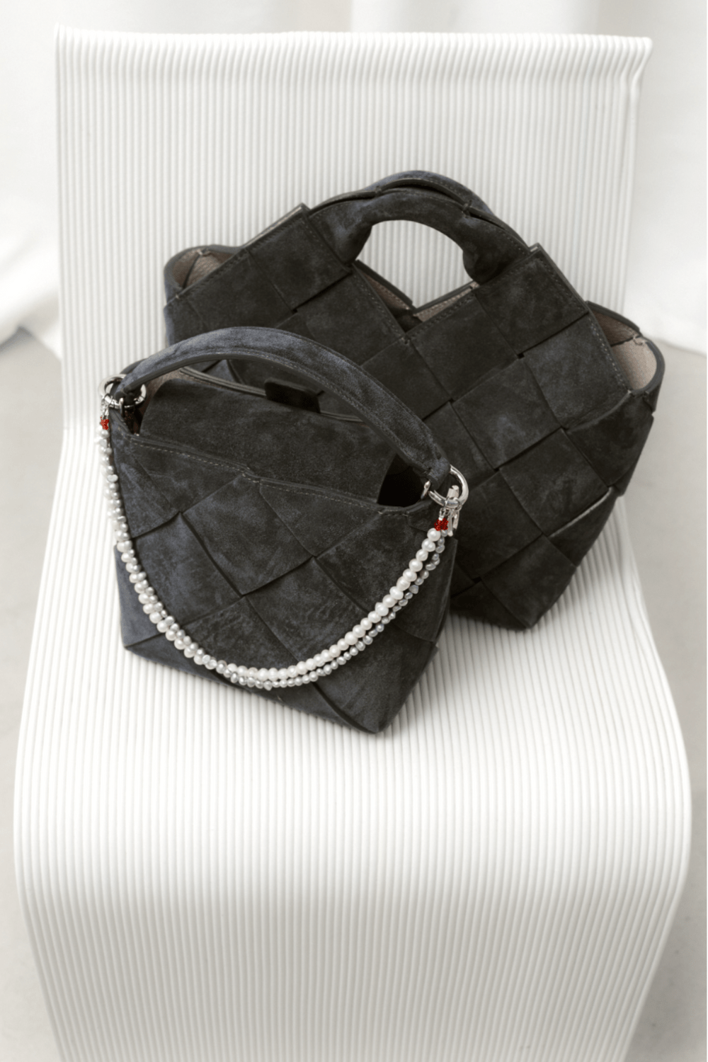 A black handbag adorned with a two-layered bag charm of freshwater pearls on a white chair