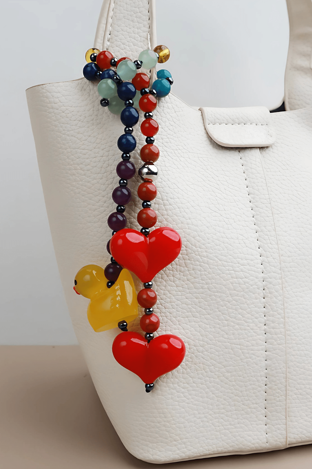 Duckie bag charm with gemstone beads, red hearts, and a yellow duck - on a white handbag.