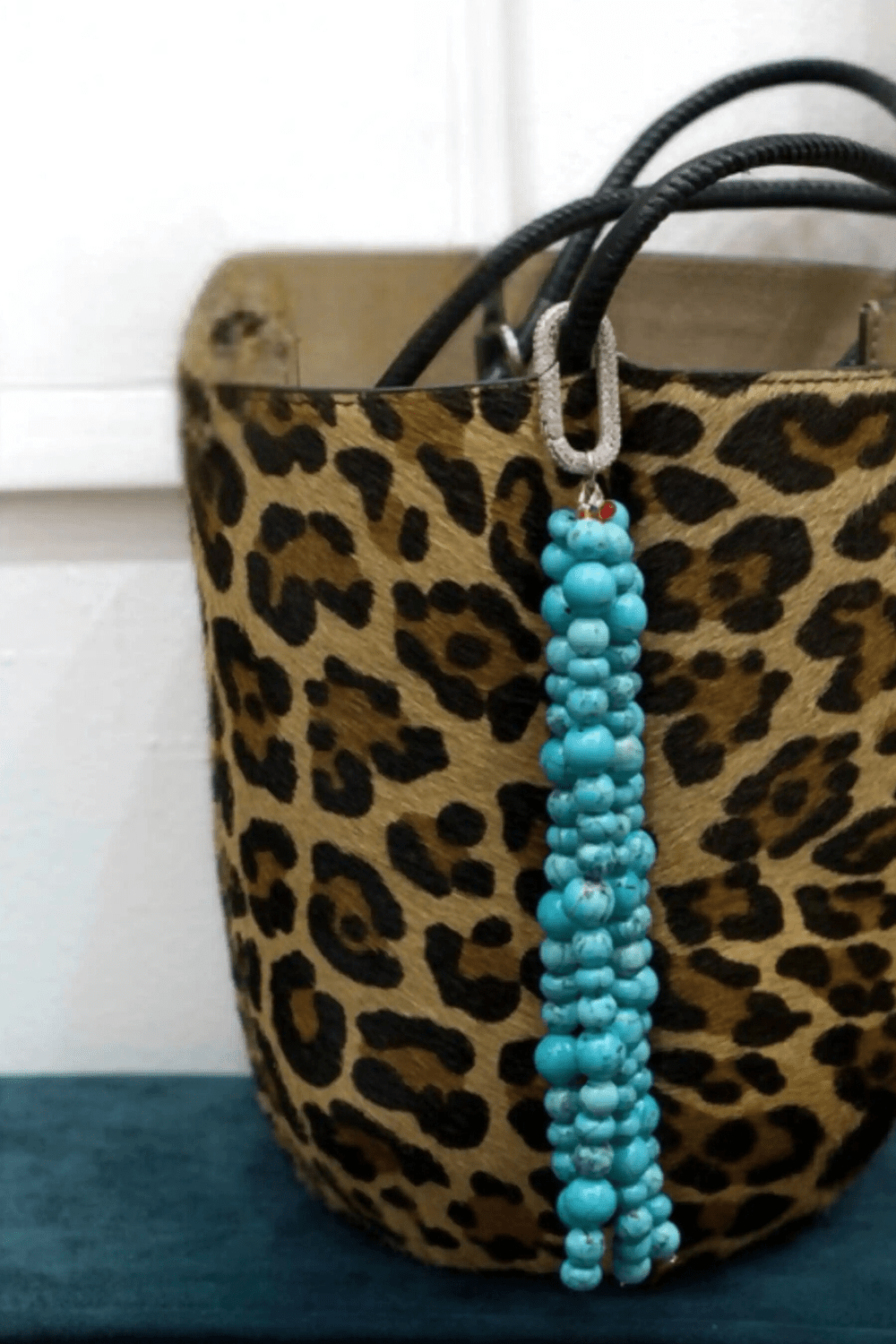 A turquoise gemstone bag charm is clipped to a leopard print handbag, showcasing the charm's size and style as a luxurious accessory.