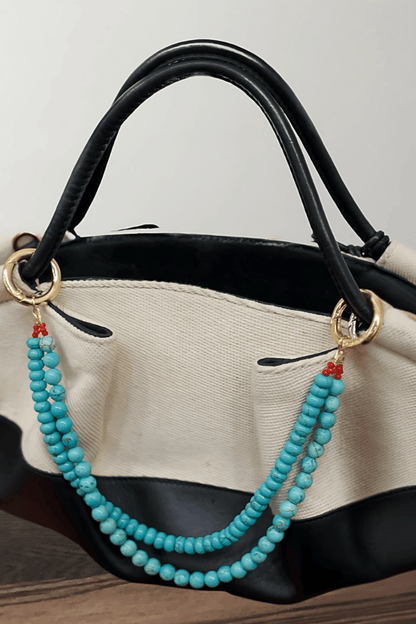 Turquoise beaded handbag charm attached to a black and beige handbag.