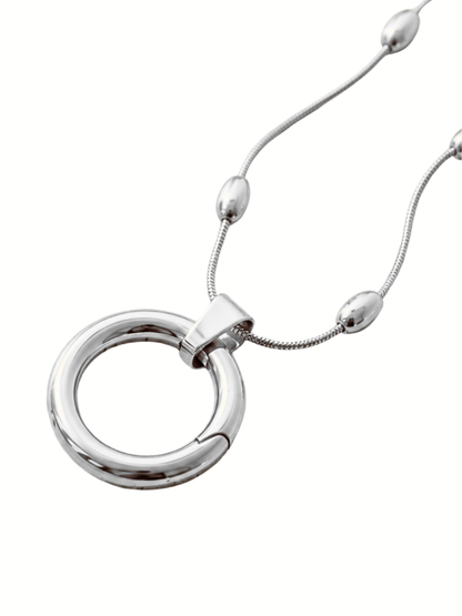 A polished silver-tone ring pendant necklace with a matching snake chain and small bead accents, shown on a plain white background.