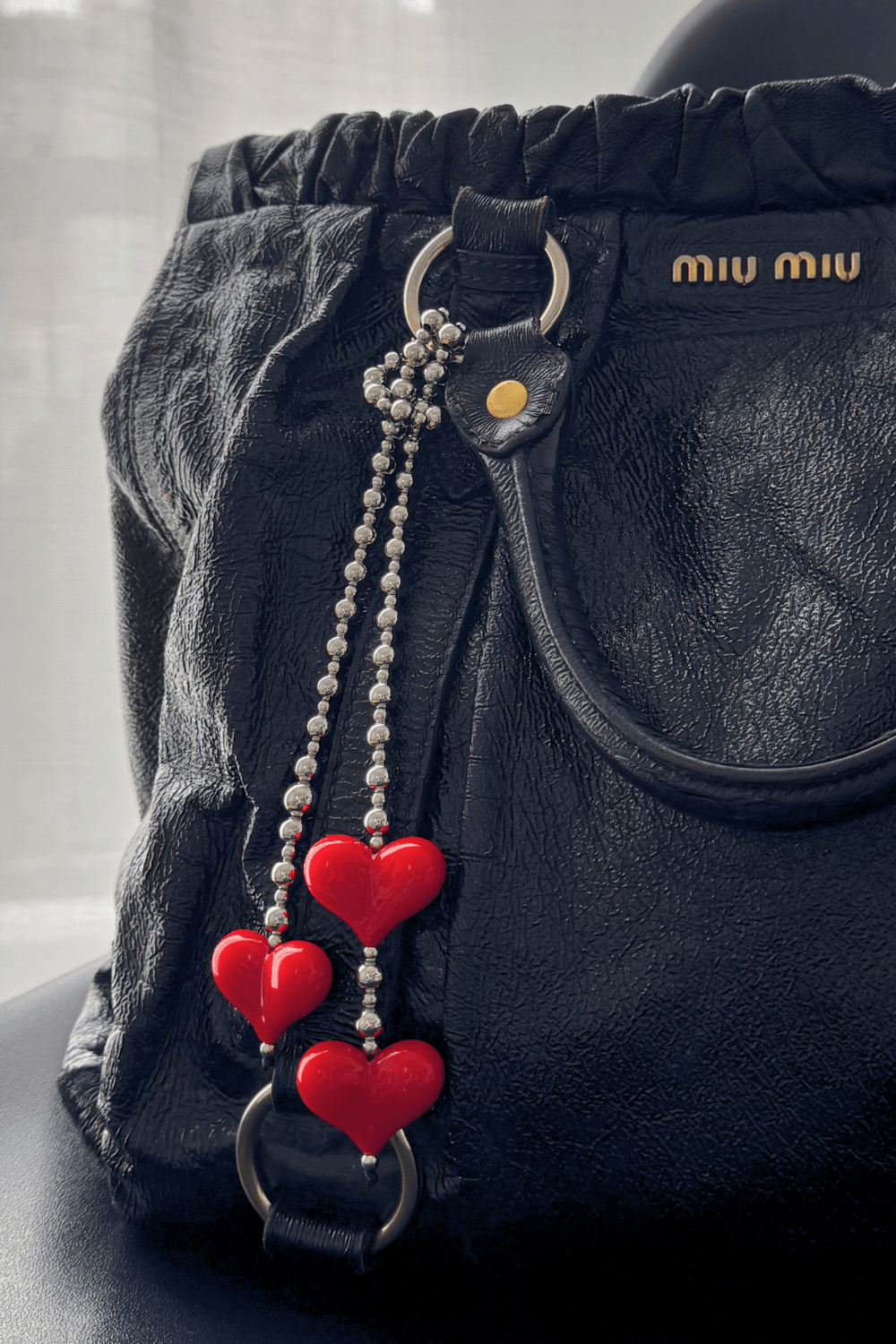 Red heart bag charm with silver beads on a black designer handbag.