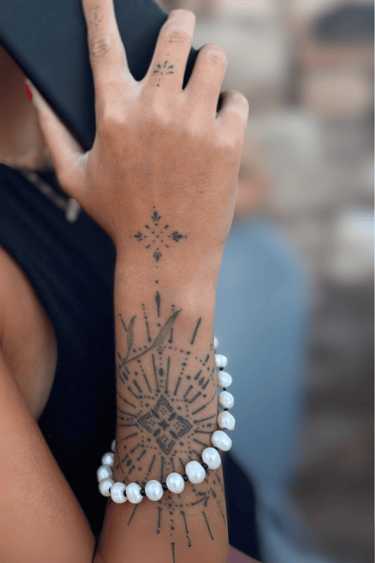 Close-up of a woman's wrist and tattooed hand, showing the Her Heritage Pearl Chain worn as a thick wrist strap or bracelet.