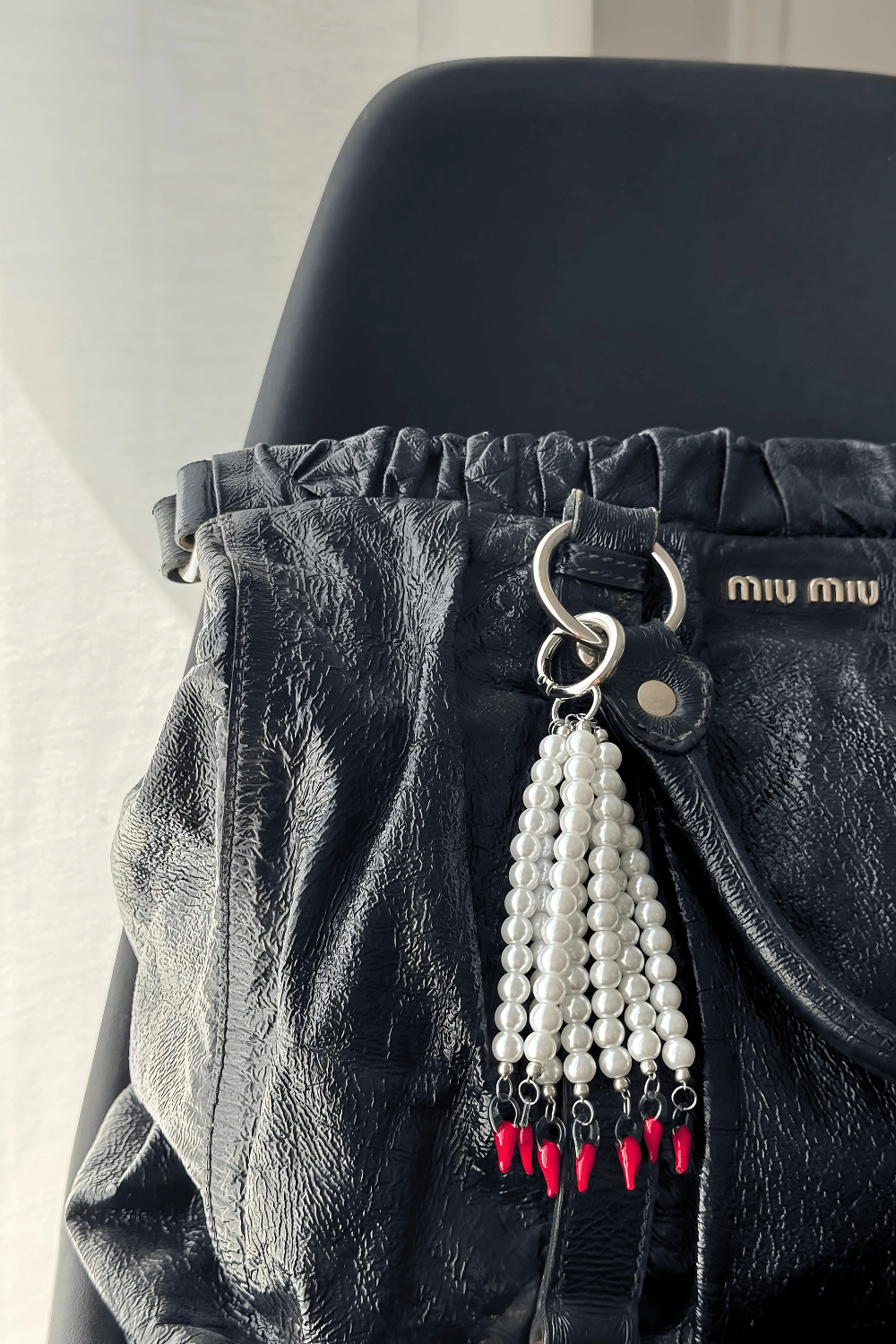 Hot Drop bag charm clipped onto a black designer handbag, showcasing glass pearls and chili peppes.