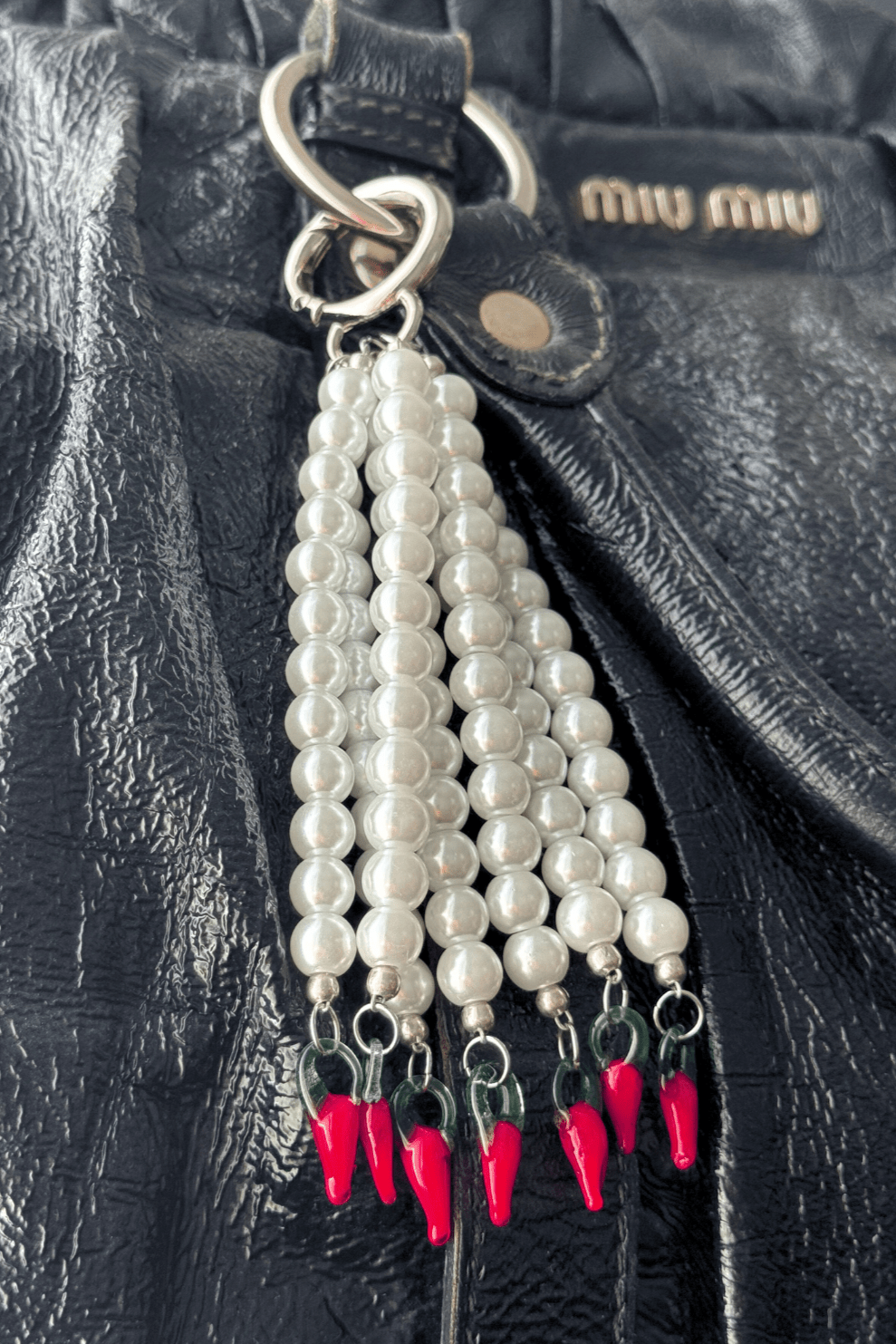 Close-up of Hot Drop keychain with pearls and red chili pepper beads, hanging from a silver o-ring clasp, attached on a designer black bag.