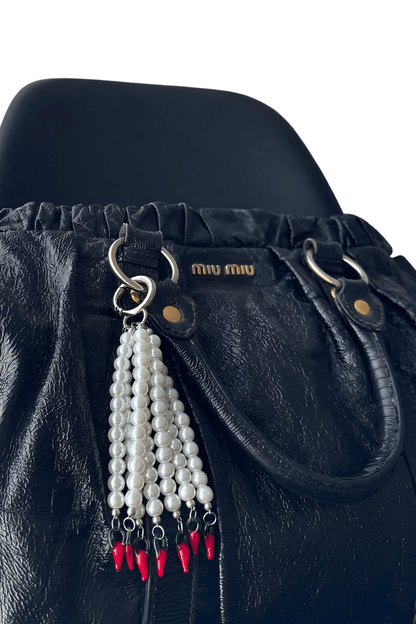 Hot Drop bag charm clipped onto a black designer handbag, showcasing pearl strands with chili pepper beads and silver o-ring clasp.