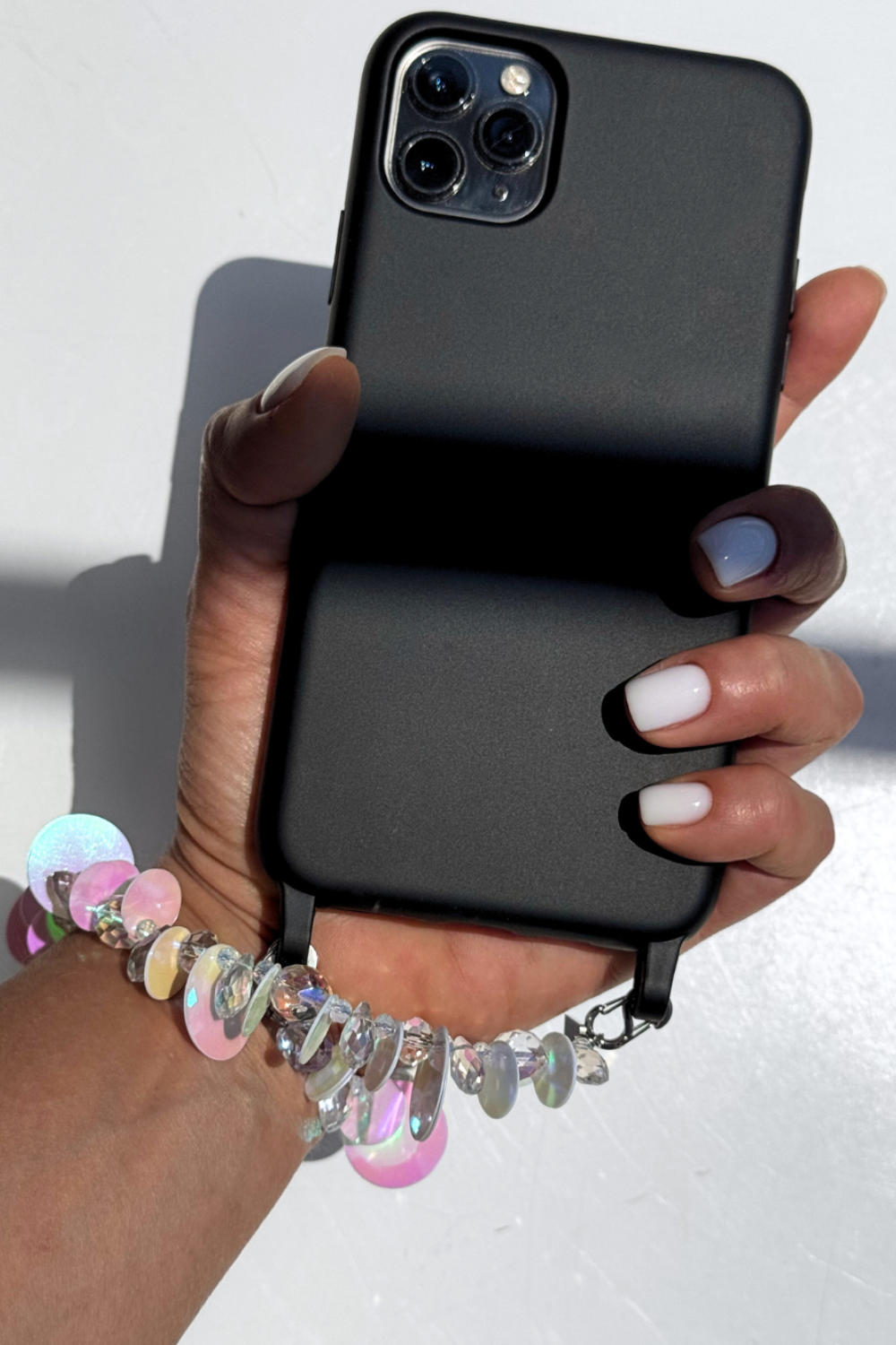 Hand holding a black phone with a Swarovski crystal phone strap on a white background