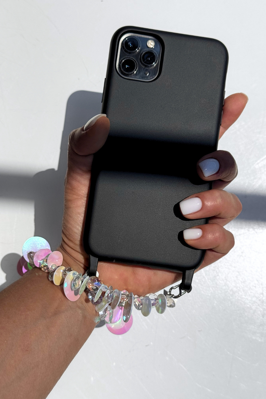 Hand holding a black phone with a Swarovski crystal phone strap on a white background