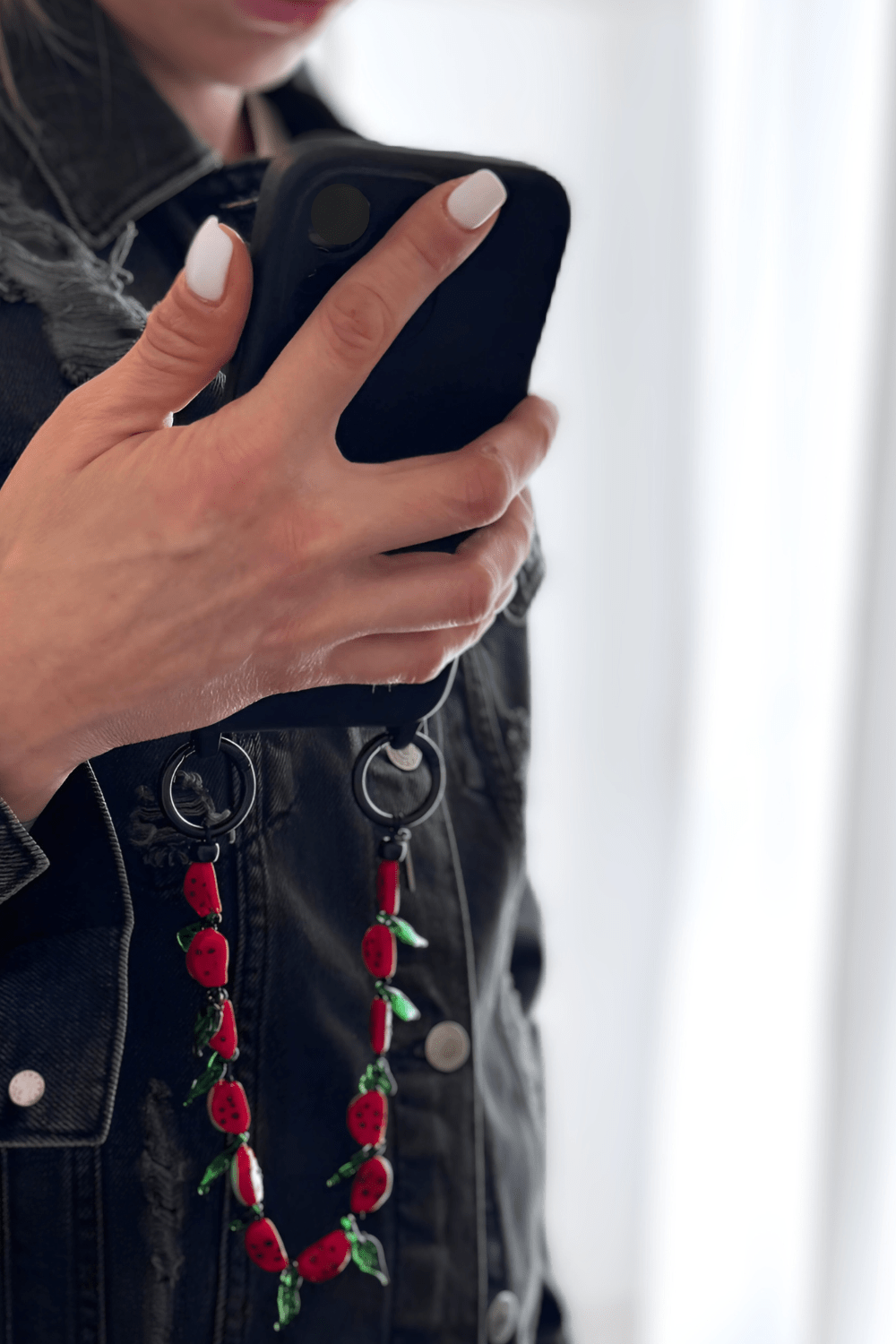 Model holding a black phone adorned with Juicy Crush beaded strap.