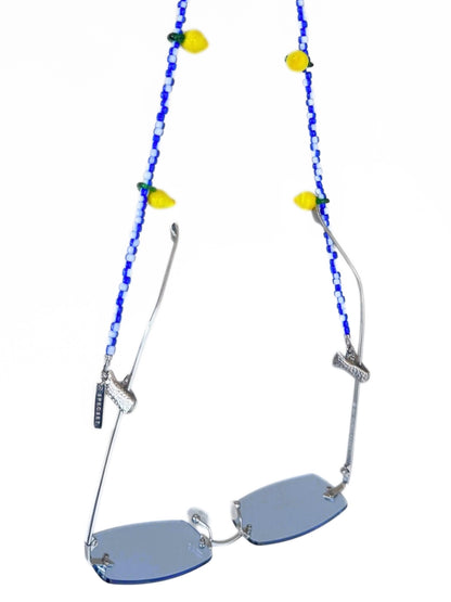 Silver rimless sunglasses with light blue lenses and a decorative blue beaded strap adorned with yellow lemon charms, shown on a white background.