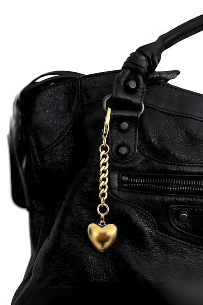 Gold heart bag charm keychain attached to black leather handbag