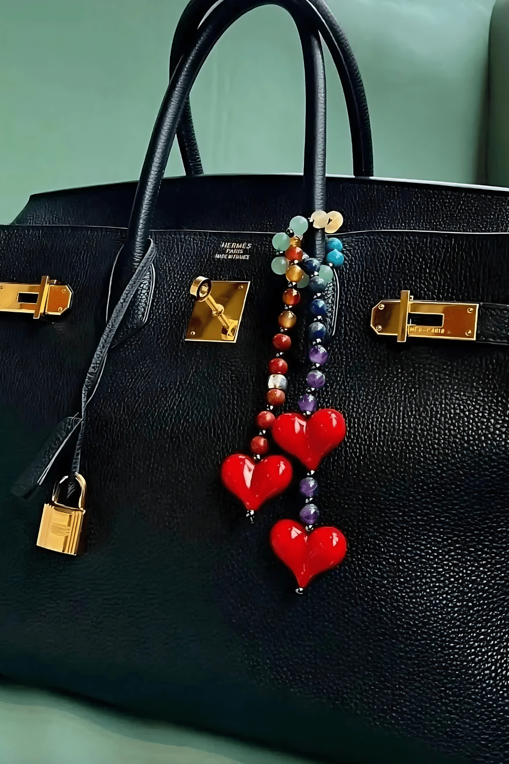 Lovlie beaded gemstone heart bag charm attached to a designer black leather handbag.