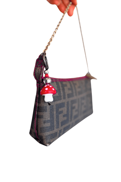 Handbag with a mushroom charm held by a hand against a white background