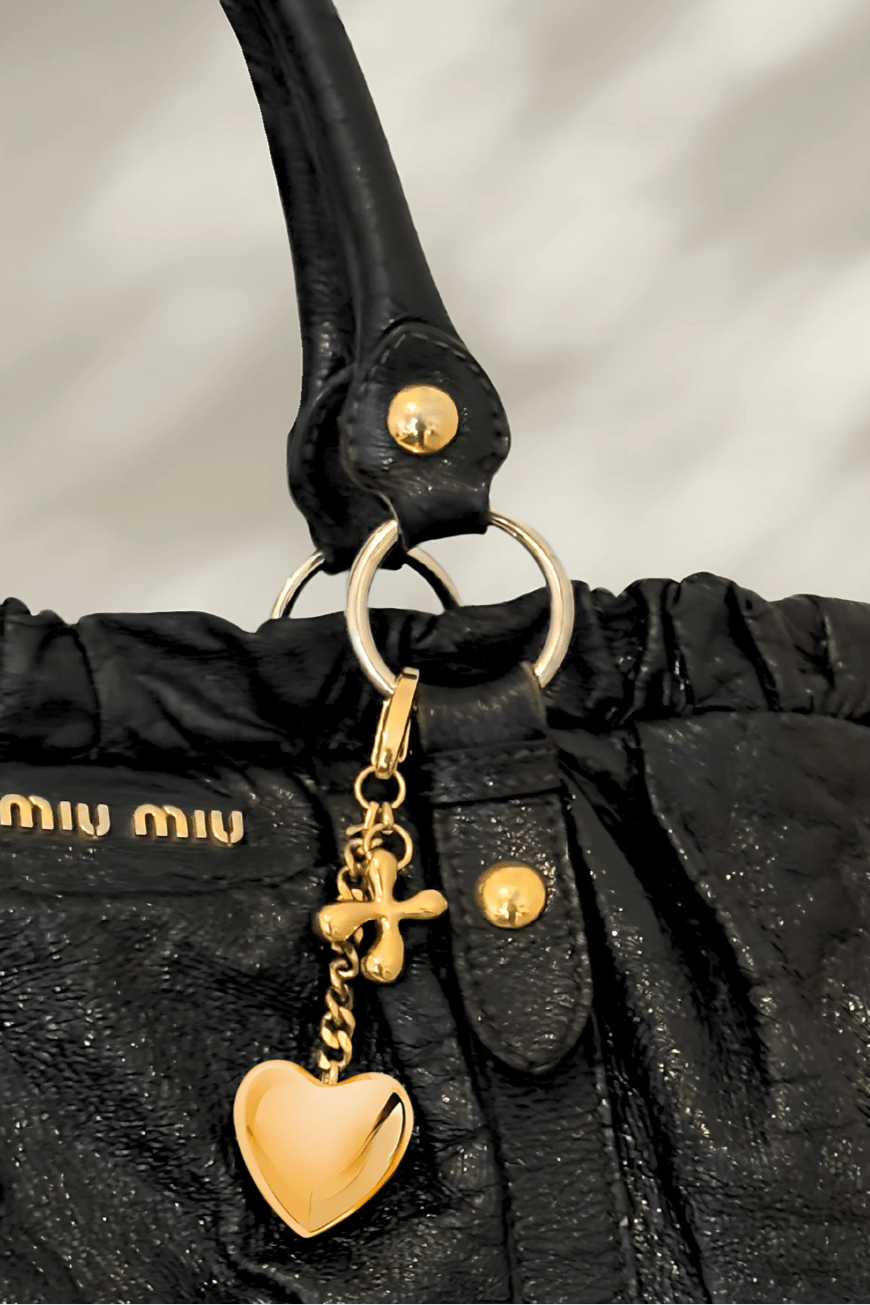 Luxury custom charm with gold heart pendant on a designer black tote bag.
