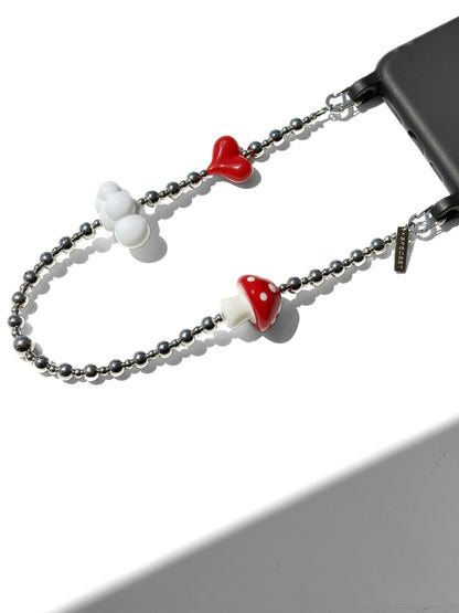 A silver beaded phone strap with decorative charms, including two red and white mushroom caps and a white cloud-shaped charm, shown attached to a black smartphone on a white background.
