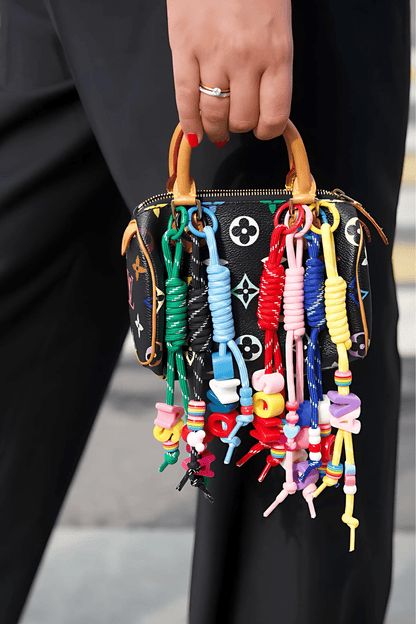 Handbag with colorful keychains held by a person wearing black pants.