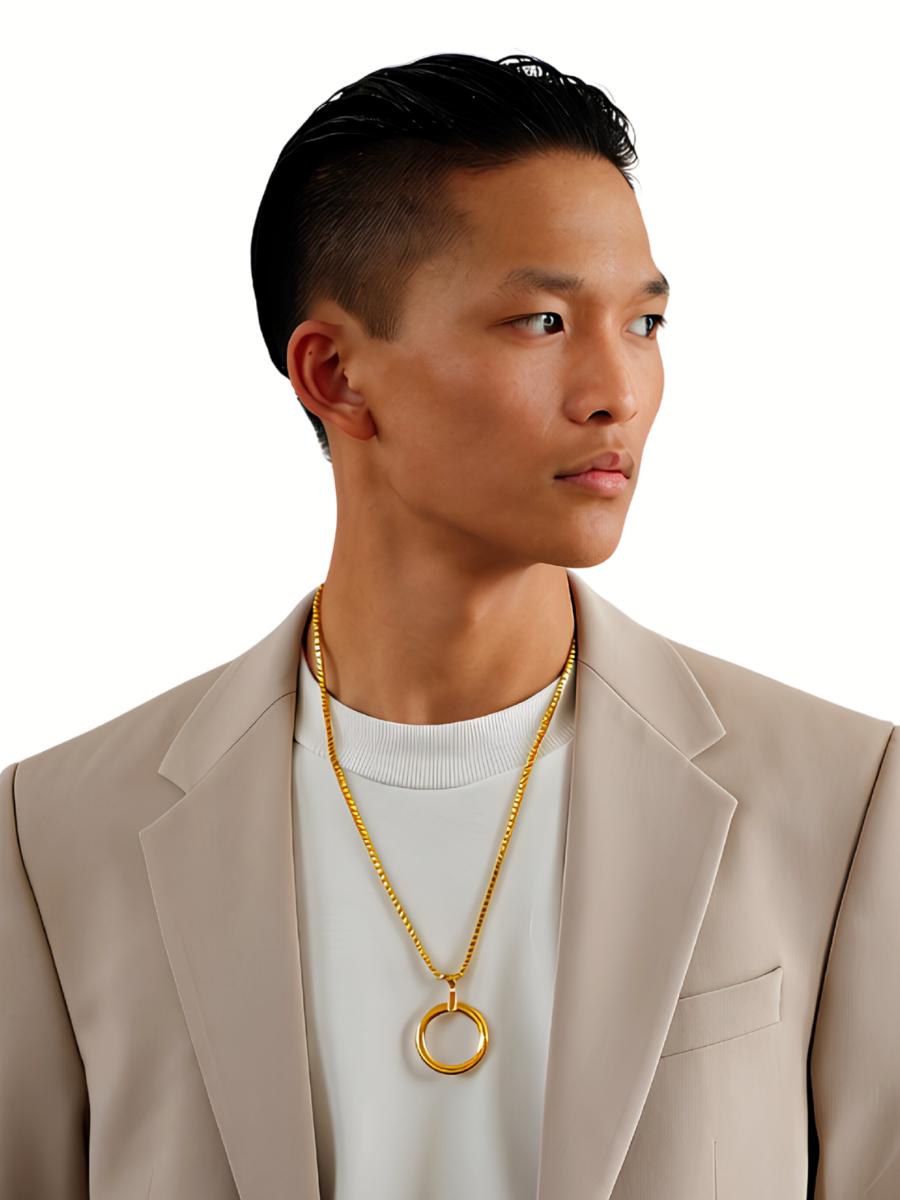 A man wearing a gold chain necklace with a large open ring pendant, styled over a white t-shirt and beige blazer, against a solid white background.