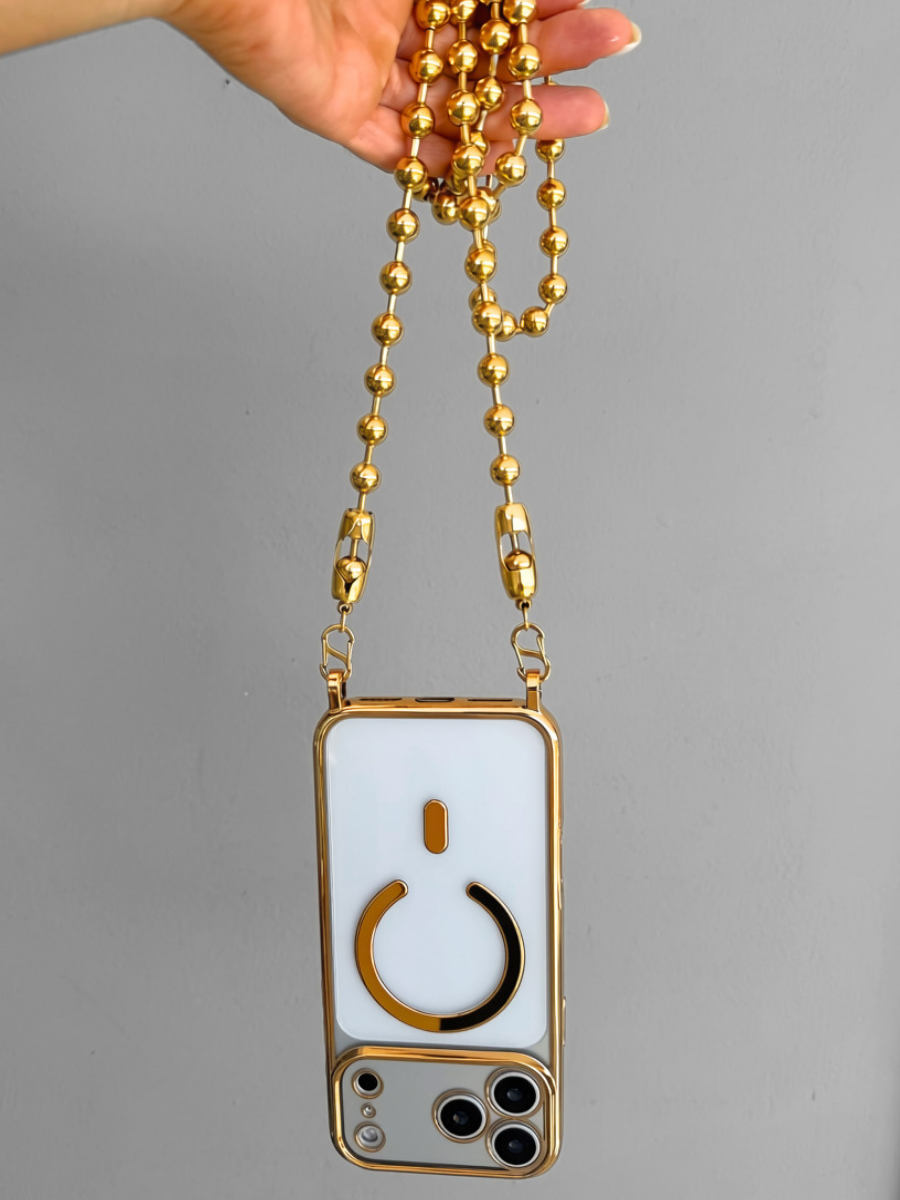 A hand holding a gold beaded crossbody phone strap with a white phone case featuring a gold power button design, set against a plain gray background.