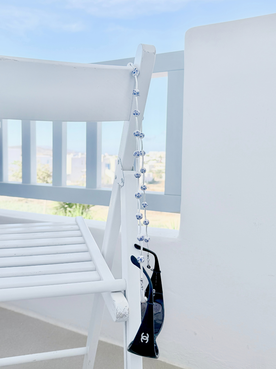 Handmade in Greece Pure Bloom eyewear chain displayed on a minimal white chair.