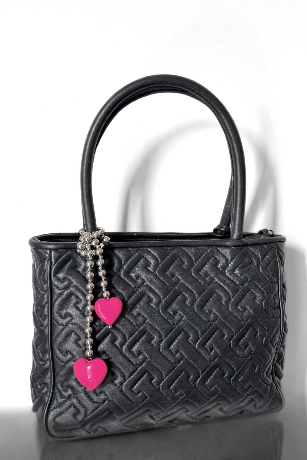 Silver beaded bag charm with pink hearts on a black handbag.