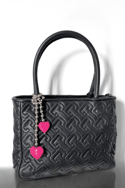 Silver beaded bag charm with pink hearts on a black handbag.