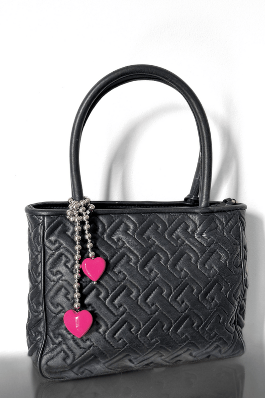 Silver beaded bag charm with pink hearts on a black handbag.