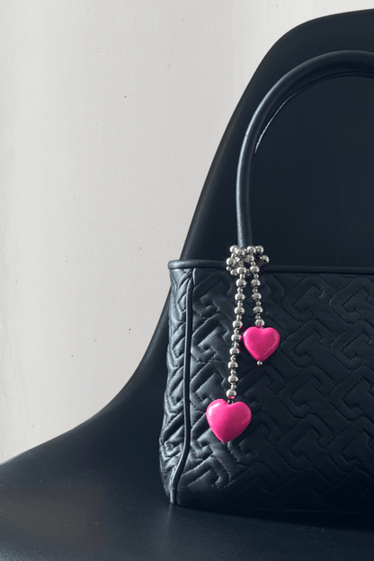Lifestyle photo of a designer handbag and a silver bead charm with pink hearts.
