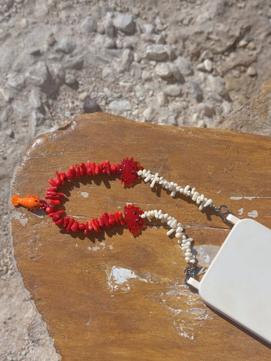 Coastal gemstone phone strap displayed on a beach table with smartphone