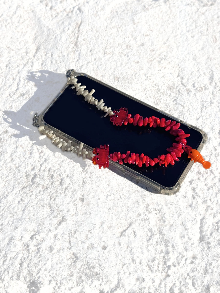 Gemstone phone strap attached to a smartphone with coastal-inspired marine charms