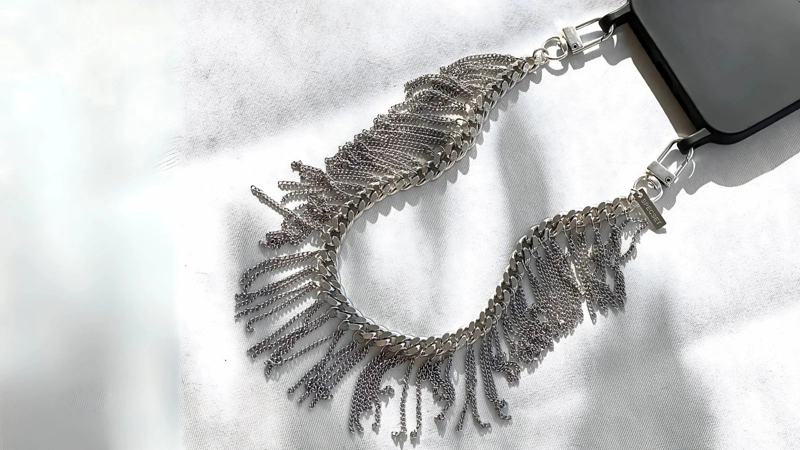 Silver fringe phone chain accessory by SPECSET, styled on white fabric.