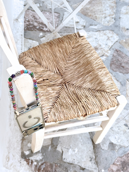 Tropic Tones beaded phone strap hanging on a wooden wicker chair against a stone background.