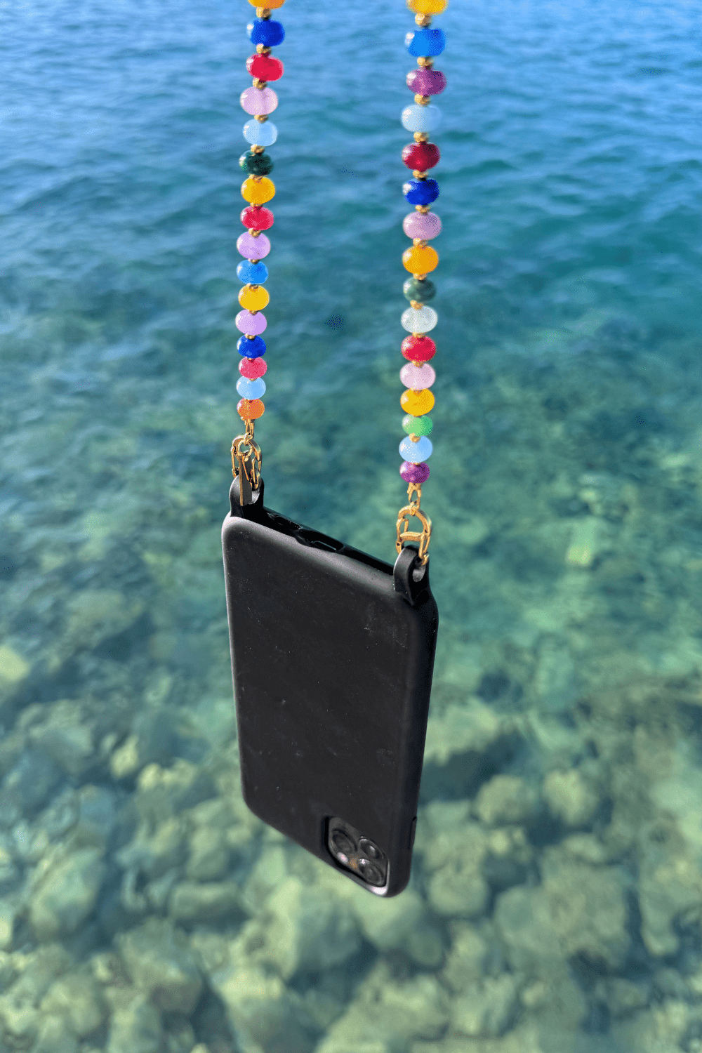 Black phone case with vivid way phone chain against a clear blue water background